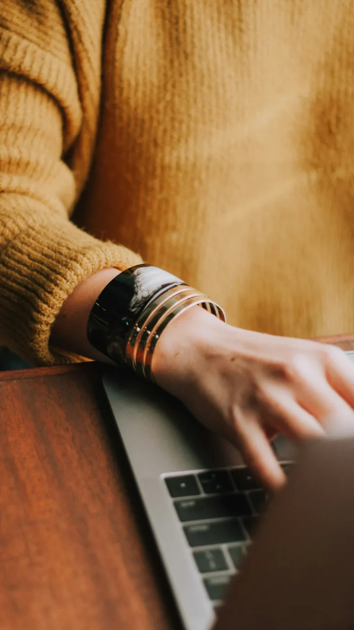 A person typing on laptop, wearing a yellow sweater and bracelets.