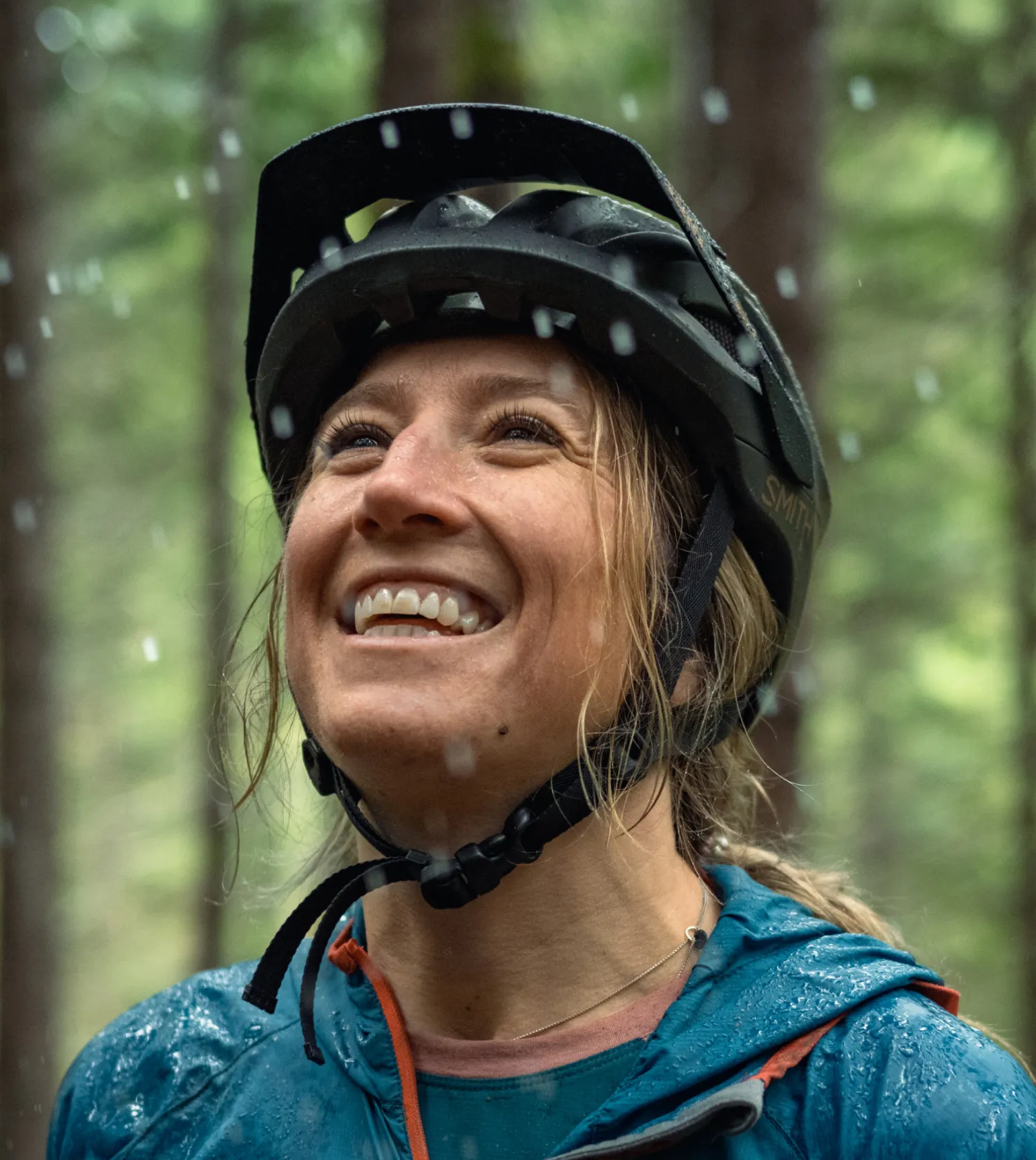 A woman in a bike helmet smiling in the rain