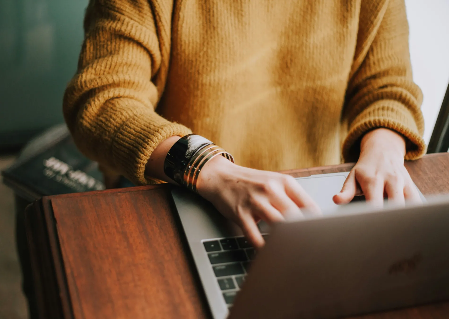 A person typing on a laptop wearing a yellow sweater.